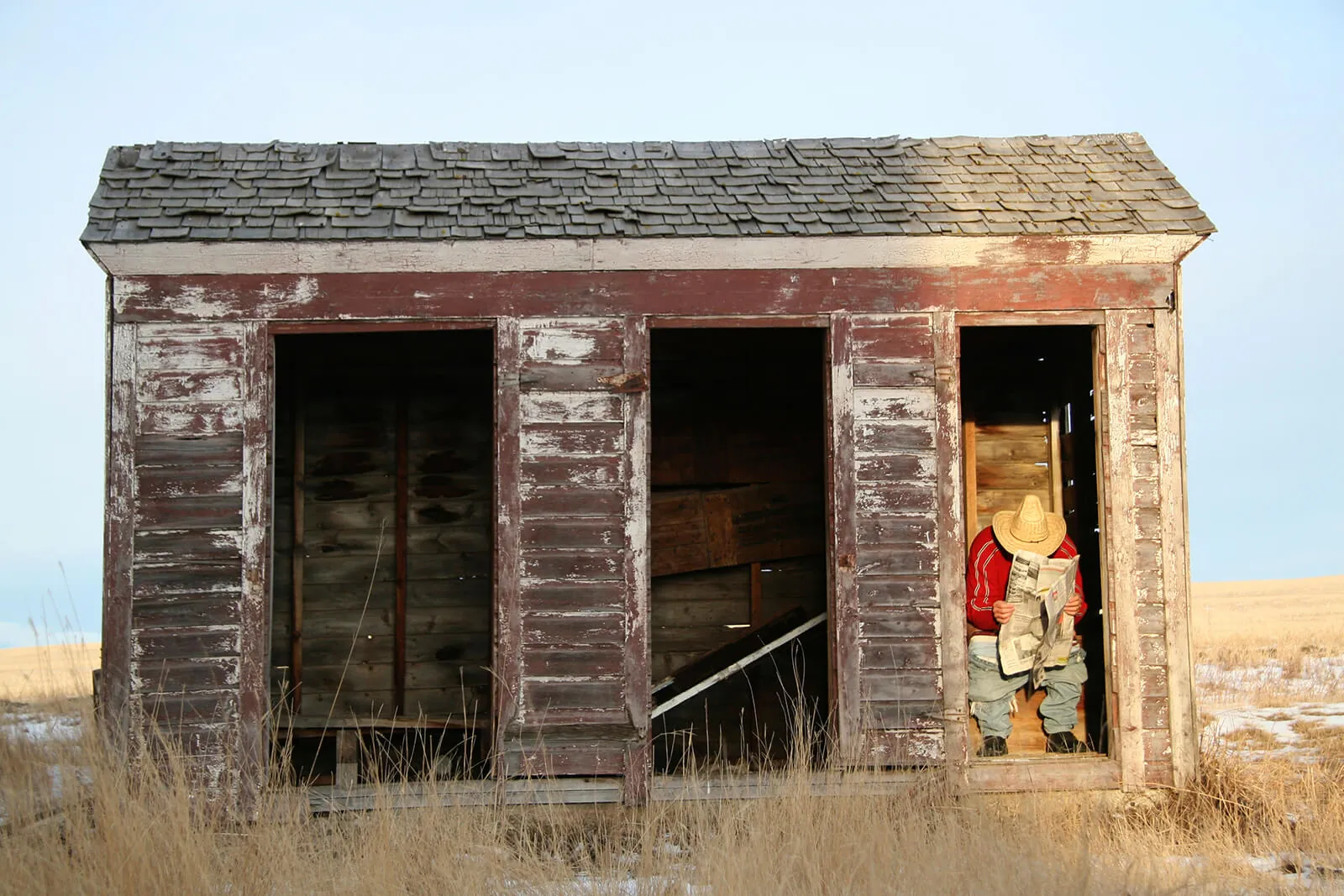 A weathered wooden outhouse in a dry field